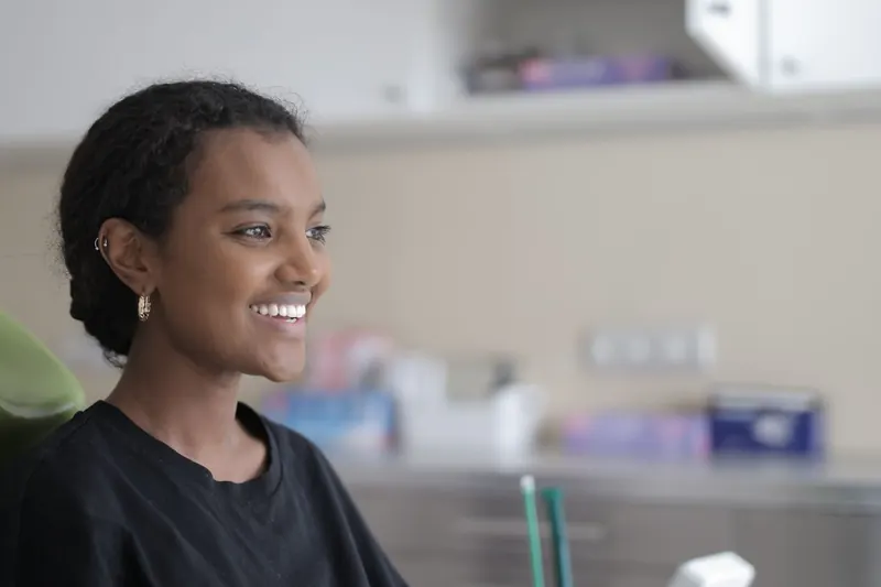 A young woman smiling as she sits back in the chair of a bright, modern dental clinic