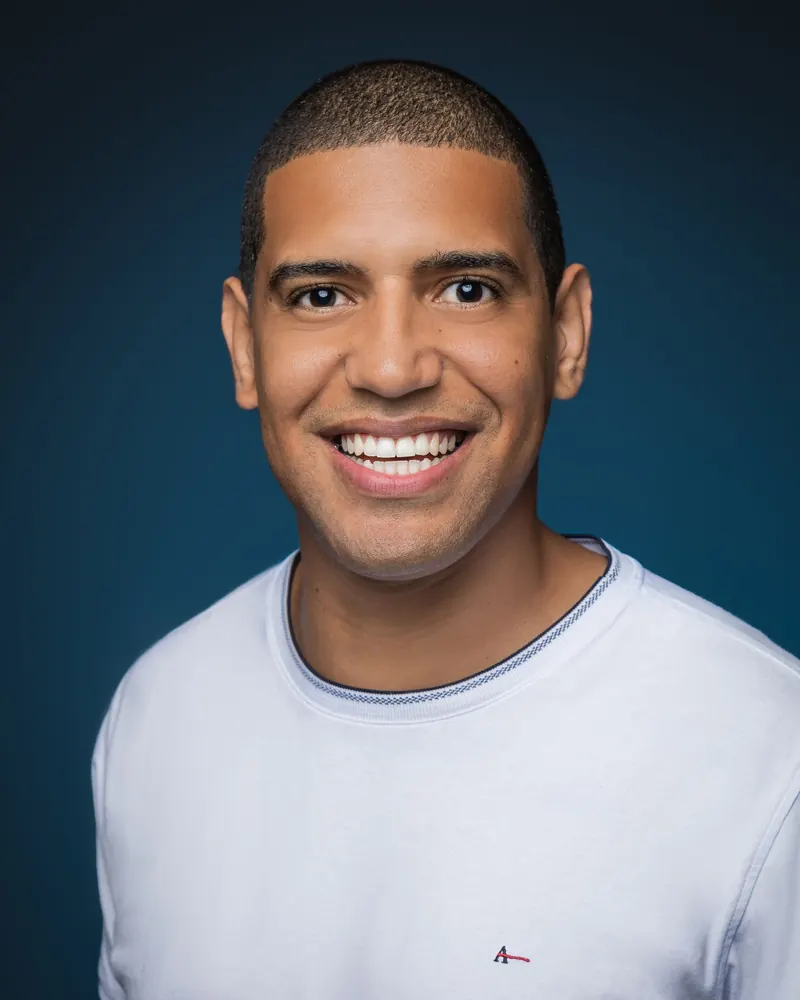 A young man in a white T-shirt with a wide, bright smile